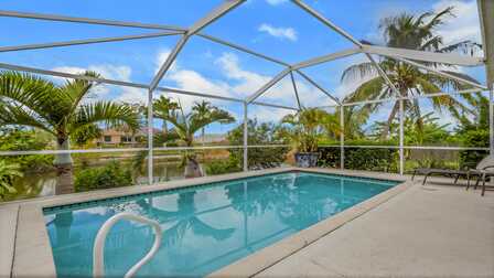Pool mit Sonnenterrasse, Screen und Blick auf Palmen und den Wasserkanal. - Traum Urlaub Florida 
