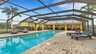 Überdachter Poolbereich mit Sitzgruppe, Sonnenliegen und Grill vor gelbem Ferienhaus. - Traum-Urlaub-Florida
