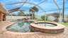 Außenbereich mit Swimmingpool und eingelassenem Whirlpool, geschützt durch einen Screen aus Aluminiumstreben und feinem Gittergewebe, umgeben von Rasen, Palmen und Sonnenliegen. - Traum-Urlaub-Florida