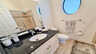 Helles Bad mit rundem Fenster, Granitwaschtisch, Dusche mit Glasabtrennung und neutralen Fliesen. - Traum-Urlaub-Florida