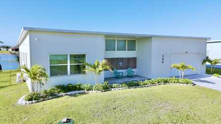 Modernes Ferienhaus am Wasser mit Palmen, gepflegtem Garten und überdachtem Eingangsbereich. - Traum Urlaub Florida 