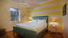 Schlafzimmer mit türkisfarbenem Bett, gelb gestreifter Wand, Deckenventilator und Fenster - Traum-Urlaub-Florida