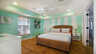 Schlafzimmer mit Korbbett, gestreifter mintfarbener Akzentwand, Deckenventilator und Fensterjalousien - Traum-Urlaub-Florida